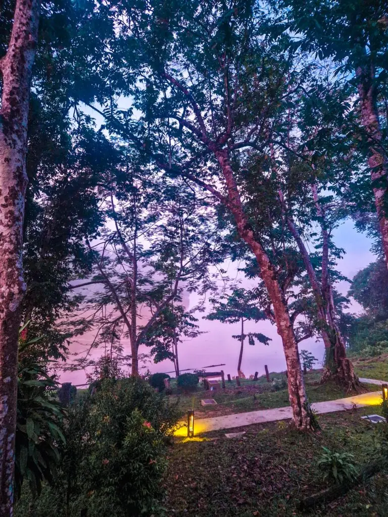 A peaceful riverside lodge surrounded by trees during a soft pink sunset, offering a tranquil end to a Kinabatangan River trip.
