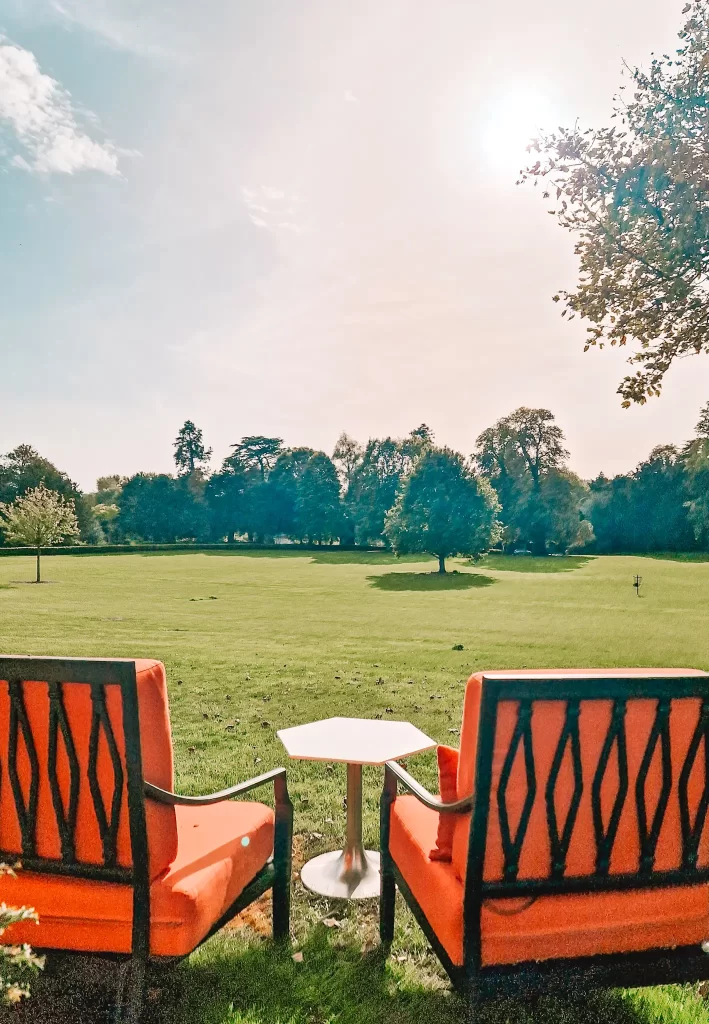 Two chairs and a table looking out over a large manicured lawn and trees