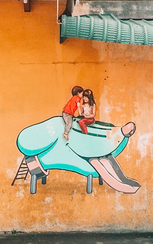 street art of two children on top of a green dogs head slide