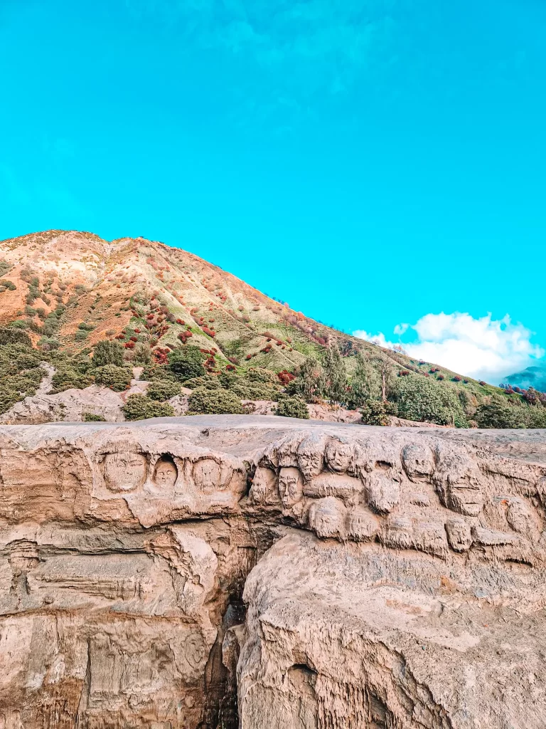 Ancient rock carvings near Mount Bromo, Indonesia, featuring detailed faces etched into the stone—a fascinating cultural site to explore on a Mount Bromo itinerary.