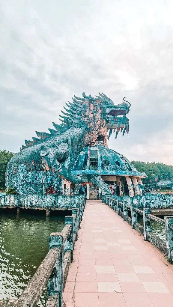 Wide shot of the iconic dragon-shaped aquarium at Hue’s abandoned Hồ Thủy Tiên water park, viewed from a weathered walkway over the lake—an unforgettable stop during 2 days in Hue.