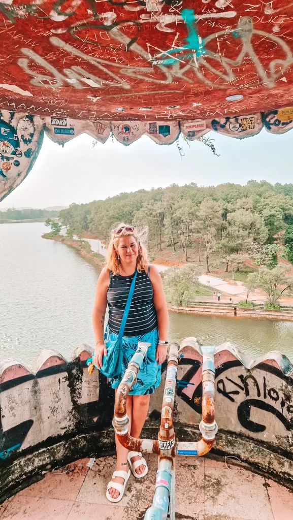 Woman standing inside a graffiti-covered tower with a view over a lake and forest, capturing the adventurous side of exploring abandoned places during 2 days in Hue.