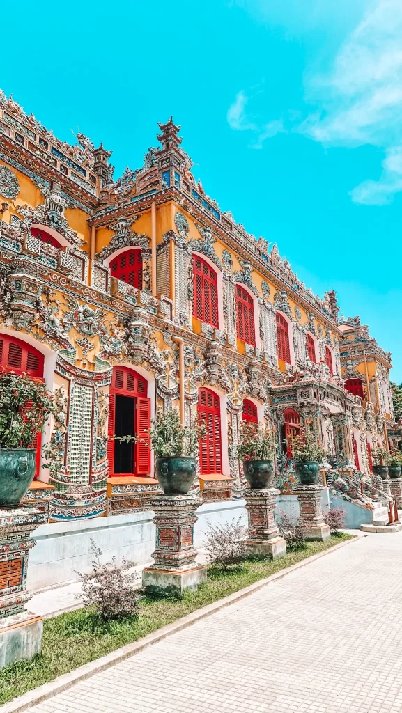 Close-up of the vibrant yellow and red exterior of the Imperial Palace, with elaborate mosaic details and large potted plants lining the walkway, capturing the rich heritage of 2 days in Hue.