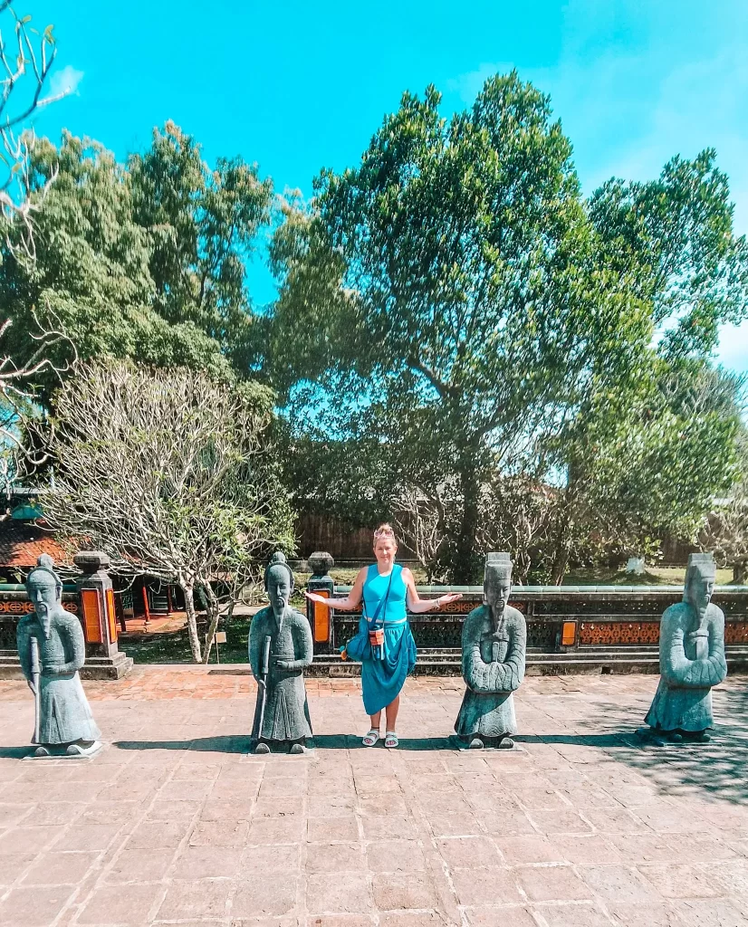  Woman posing between stone statues of ancient mandarins at an imperial tomb site, showcasing the historic and cultural richness found during 2 days in Hue.