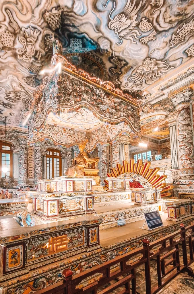 Intricately decorated royal tomb interior featuring a golden statue of Emperor Khai Dinh, surrounded by colorful mosaics and an elaborately painted ceiling, a must-visit masterpiece during 2 days in Hue.