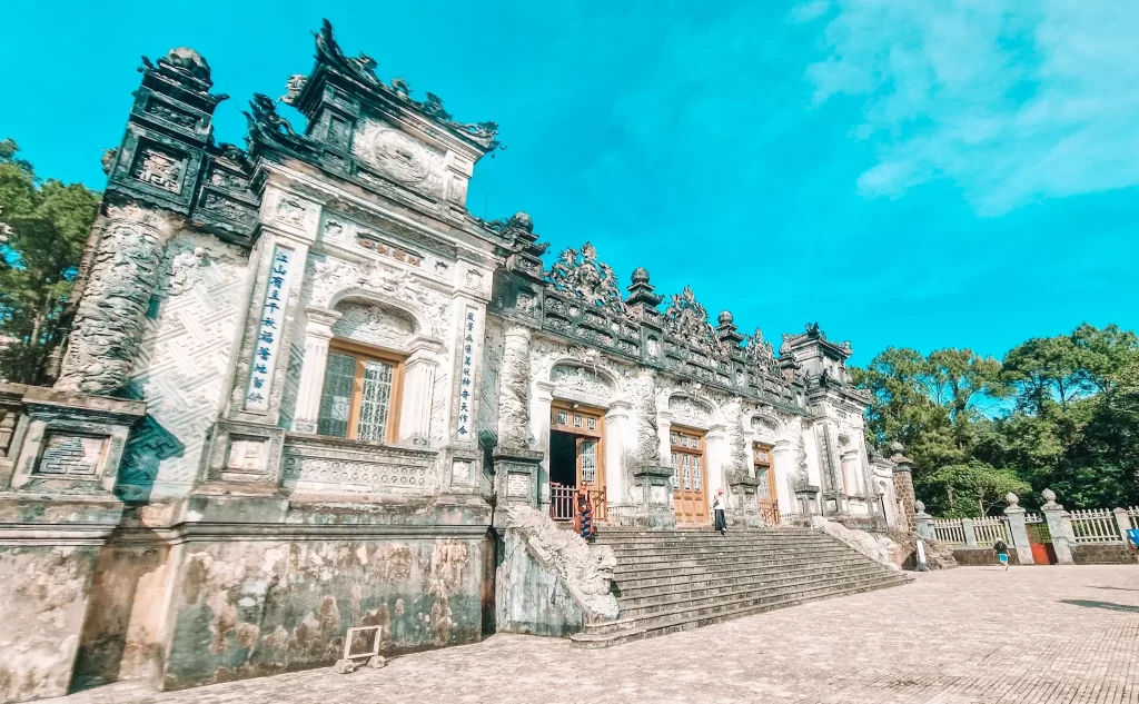Ornate stone facade of the Khai Dinh Tomb with intricate carvings and grand staircases under a bright blue sky, a stunning architectural highlight to visit during 2 days in Hue.