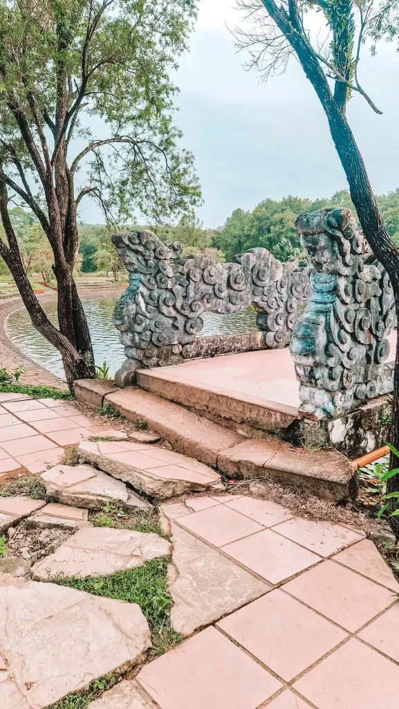 Cracked and uneven stone path leading to an ornate, weathered dragon-carved bridge by a pond, capturing the haunting beauty of forgotten sites explored during 2 days in Hue.