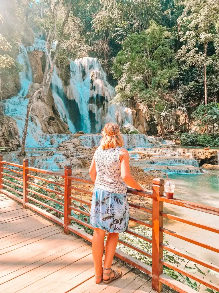 A woman gazes at the cascading tiers of Kuang Si Waterfalls from a wooden viewing deck, a breathtaking natural wonder and one of the best things to do in Luang Prabang.