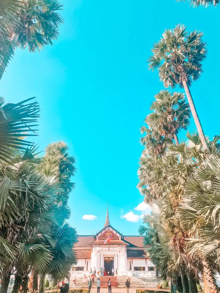 The Royal Palace Museum in Luang Prabang, framed by tall palm trees under a bright blue sky, offering cultural insights as one of the best things to do in Luang Prabang.