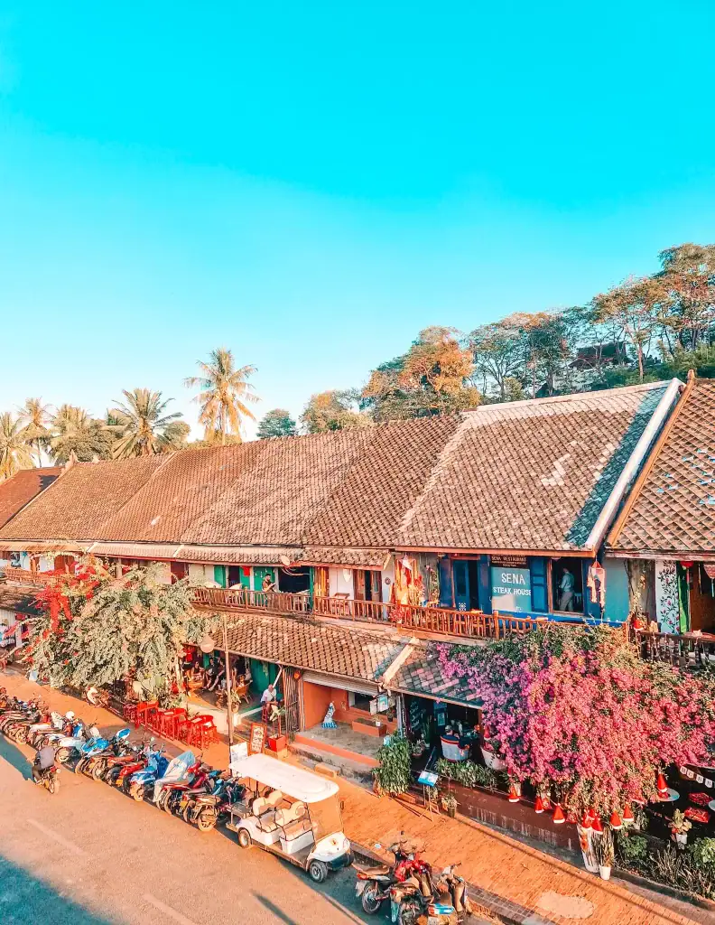A vibrant street scene in Luang Prabang with colorful houses, motorbikes, and blooming flowers, capturing the lively atmosphere that's part of the best things to do in Luang Prabang.