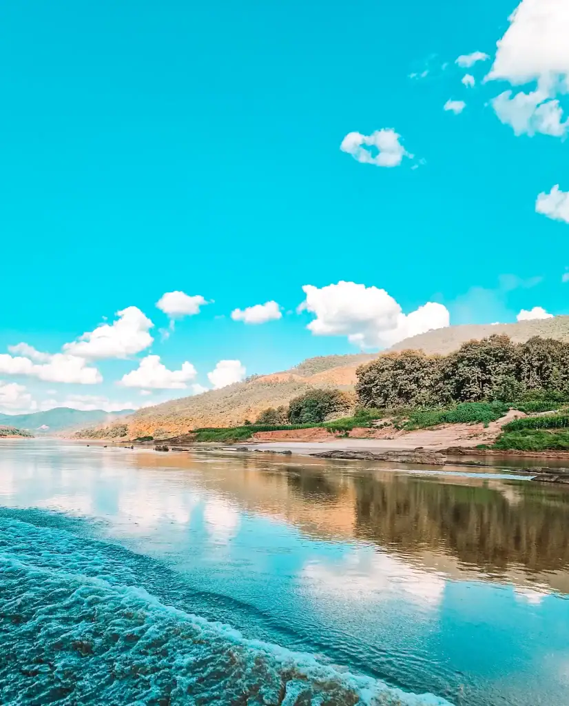 View from a boat of the wake of the boat and green hillsides, which are reflected in the river water.