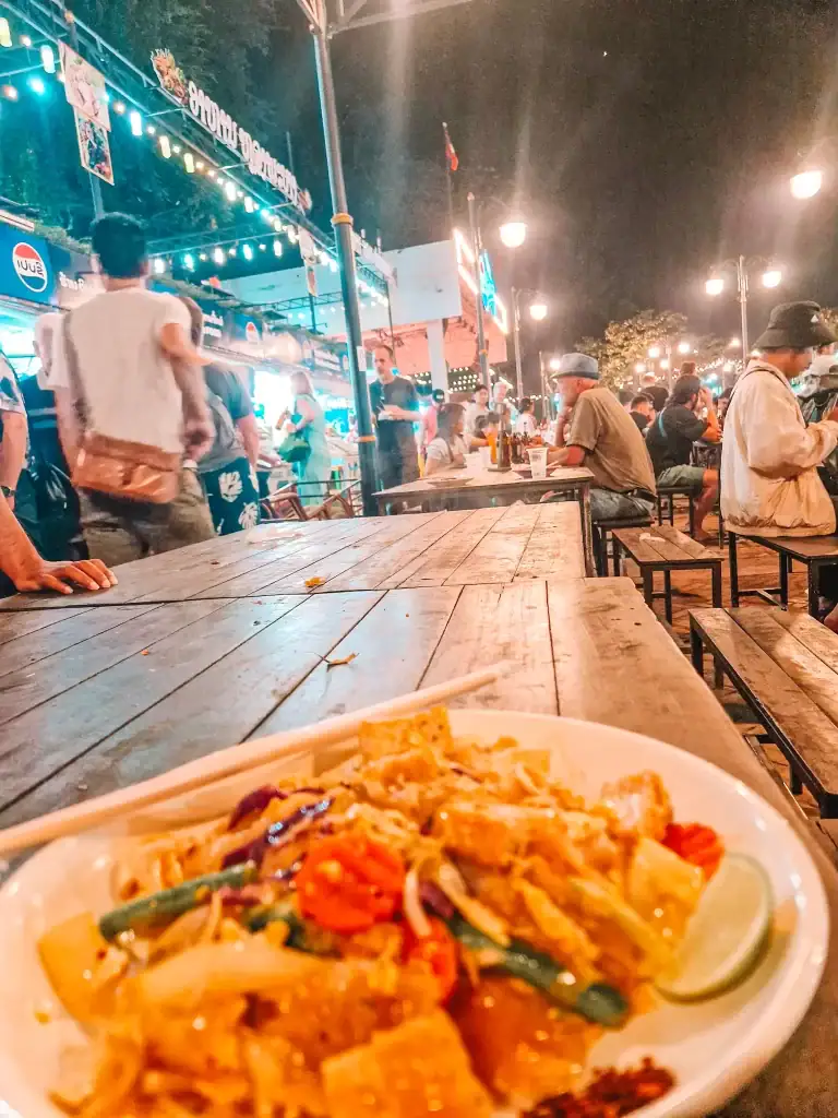 A close-up of a vibrant noodle dish at the Luang Prabang night market, surrounded by locals and tourists—exploring this food scene is one of the best things to do in Luang Prabang.