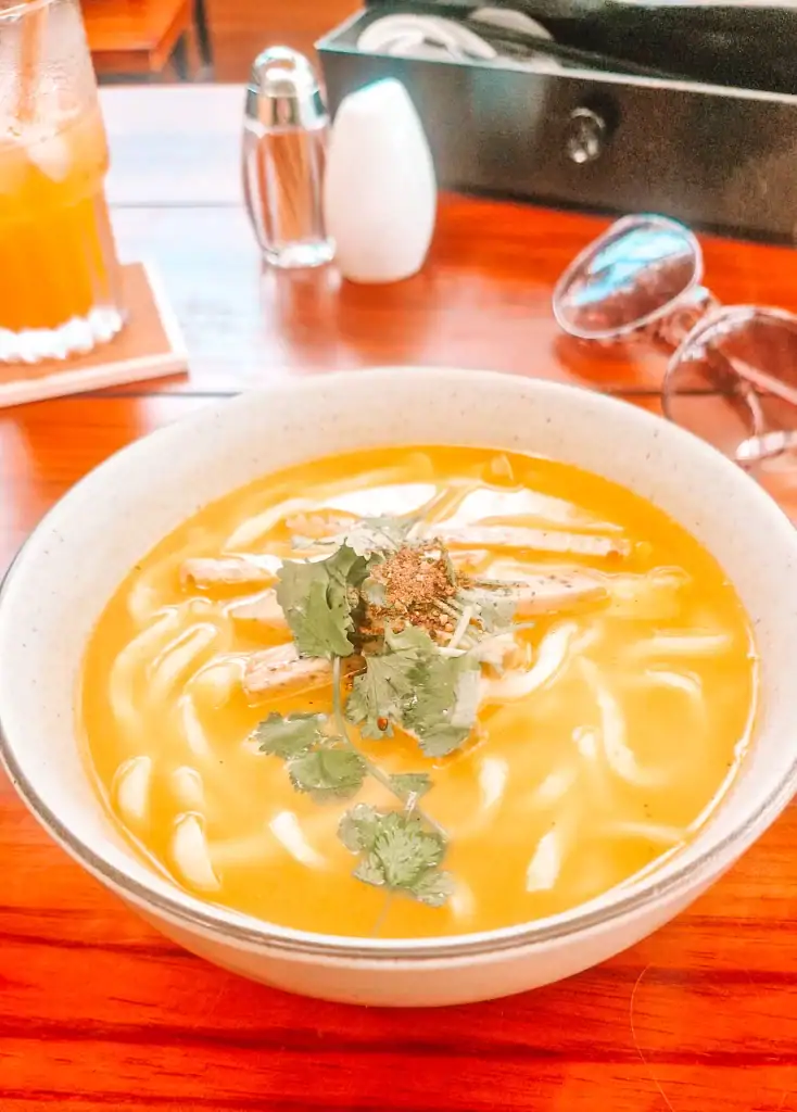 A hearty bowl of vegan soup with noodles, topped with fresh cilantro, enjoyed at one of the best vegan restaurants in Da Nang, alongside a glass of iced tea and casual table setup.