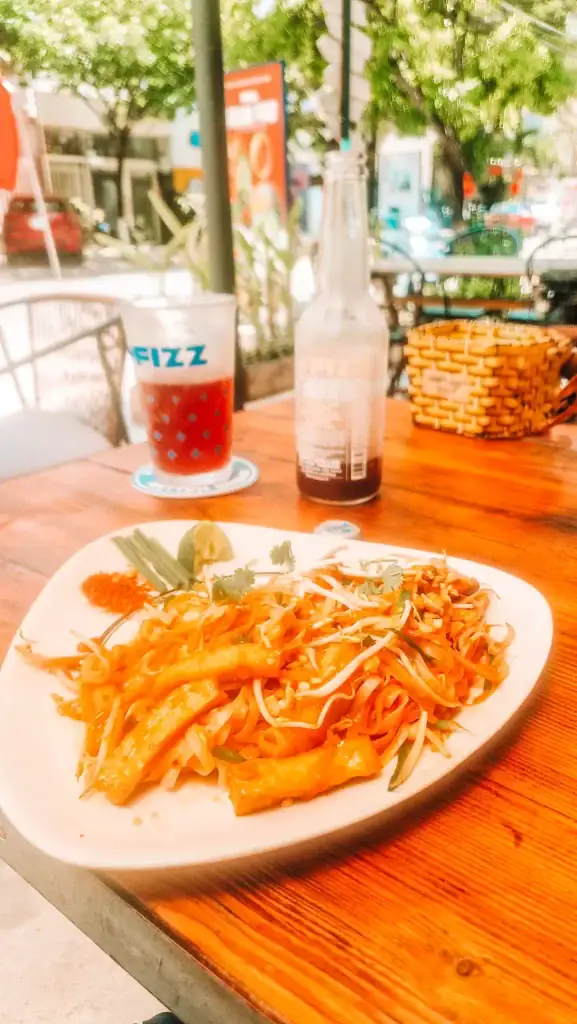 Outdoor table at one of the best vegan restaurants in Da Nang featuring a plate of vegan pad thai with tofu and bean sprouts, paired with a refreshing drink.