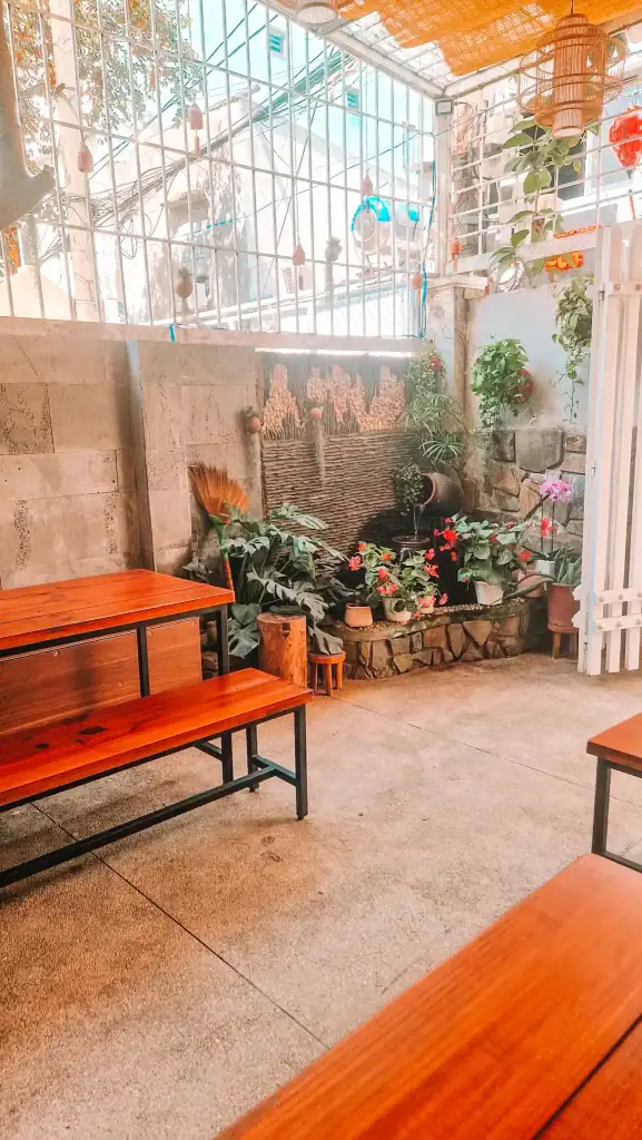 Cozy outdoor seating area at one of the best vegan restaurants in Da Nang, featuring wooden benches, potted plants, and a decorative water fountain under a partially open roof.