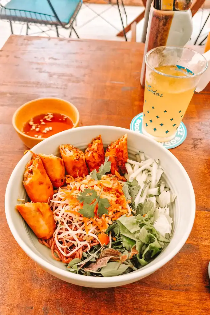 Bowl of vegan vermicelli noodles topped with crispy spring rolls, fresh herbs, and shredded vegetables, paired with a dipping sauce and a refreshing drink at one of the best vegan restaurants in Da Nang.
