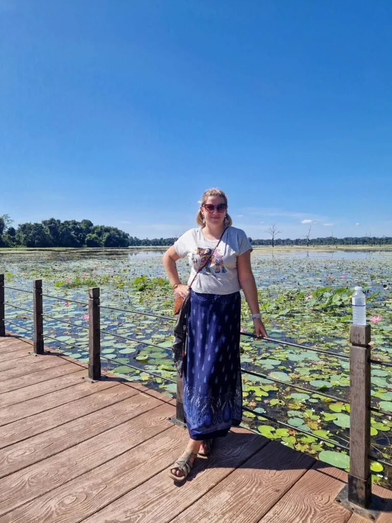 A solo female traveller stands on a wooden boardwalk overlooking a lotus-filled lake, enjoying the peaceful beauty of nature.