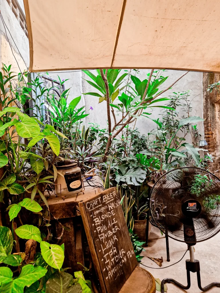 A cozy corner in Battambang featuring a rustic craft beer menu with options like Blonde, IPA, and Amber, surrounded by lush plants and vintage decor—perfect for relaxing during 2 days in Battambang.