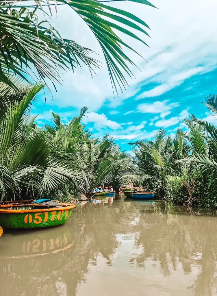 A lush waterway surrounded by dense palm trees with round basket boats floating along the calm river in Hoi An. Taking a basket boat tour through the coconut palm groves is one of the best things to do in Hoi An for an authentic local experience.