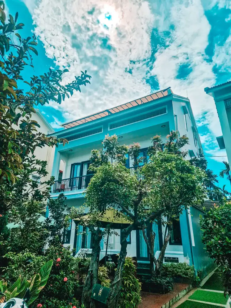 Modern guesthouse in Hoi An surrounded by lush gardens and tropical plants, with balconies and large windows under a dramatic blue sky—an inviting place to stay on any Central Vietnam itinerary.