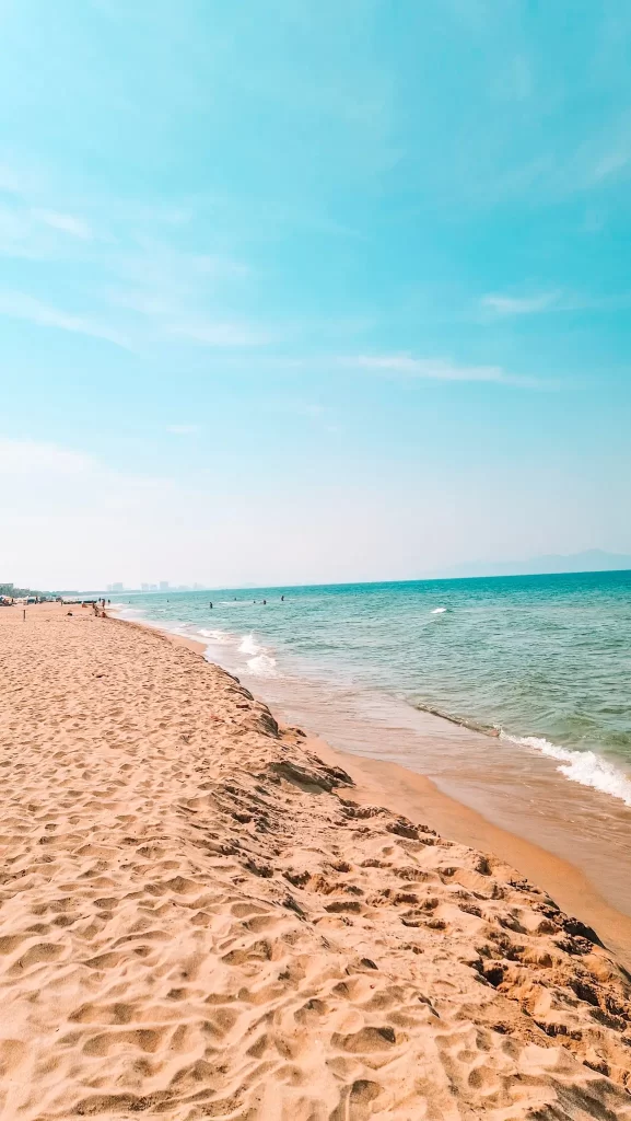 A serene beach scene with gentle waves and distant green mountains under a bright blue sky in Hoi An, Vietnam. Relaxing at the beach is definitely one of the best things to do in Hoi An for nature lovers.