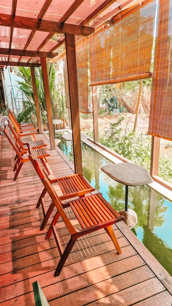 A tranquil outdoor seating area with wooden chairs and a shaded koi pond, ideal for relaxing during cultural or wellness-focused day trips from Hoi An.