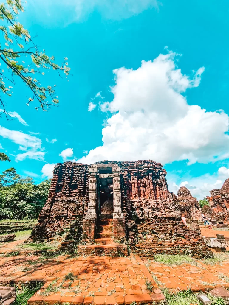 An ancient red-brick temple with a weathered entrance and stone carvings, located in a lush forest—one of the culturally rich sites explored during day trips from Hoi An.
