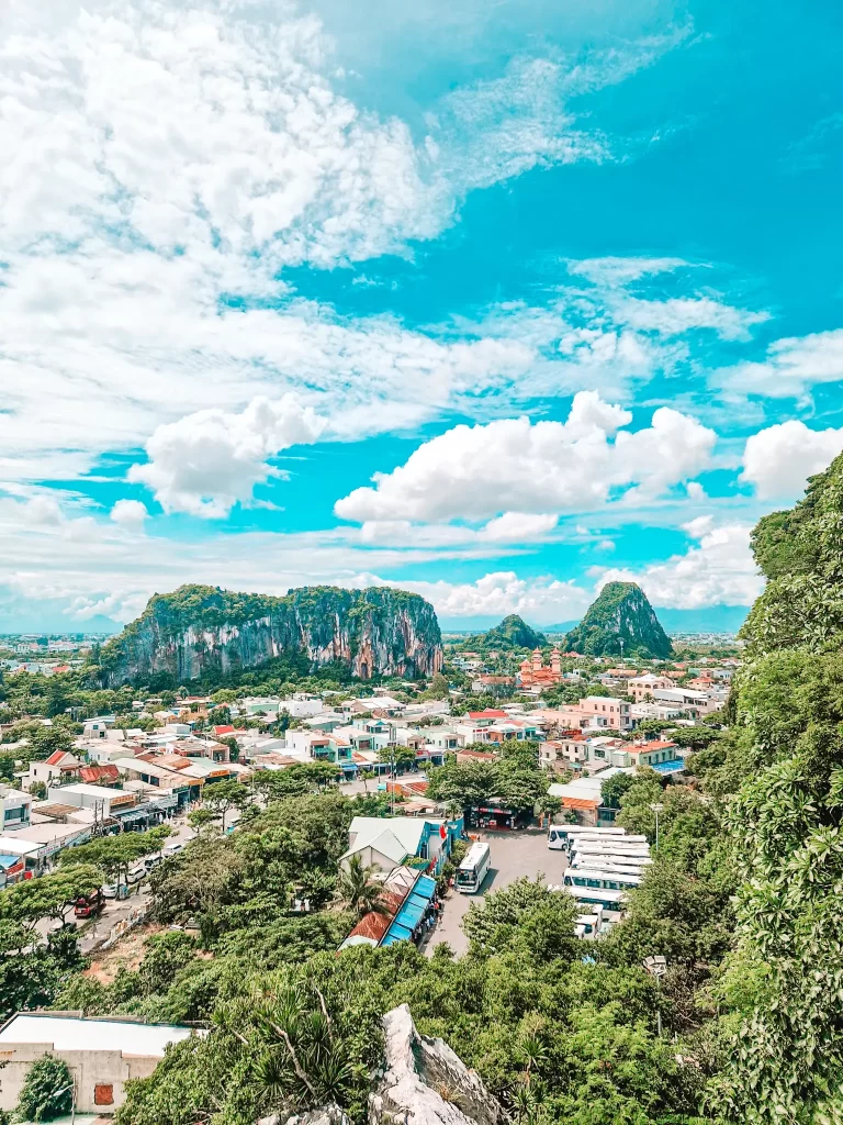 A panoramic view of a vibrant town nestled below the Marble Mountains, a popular destination offering caves, pagodas, and scenic vistas on day trips from Hoi An.