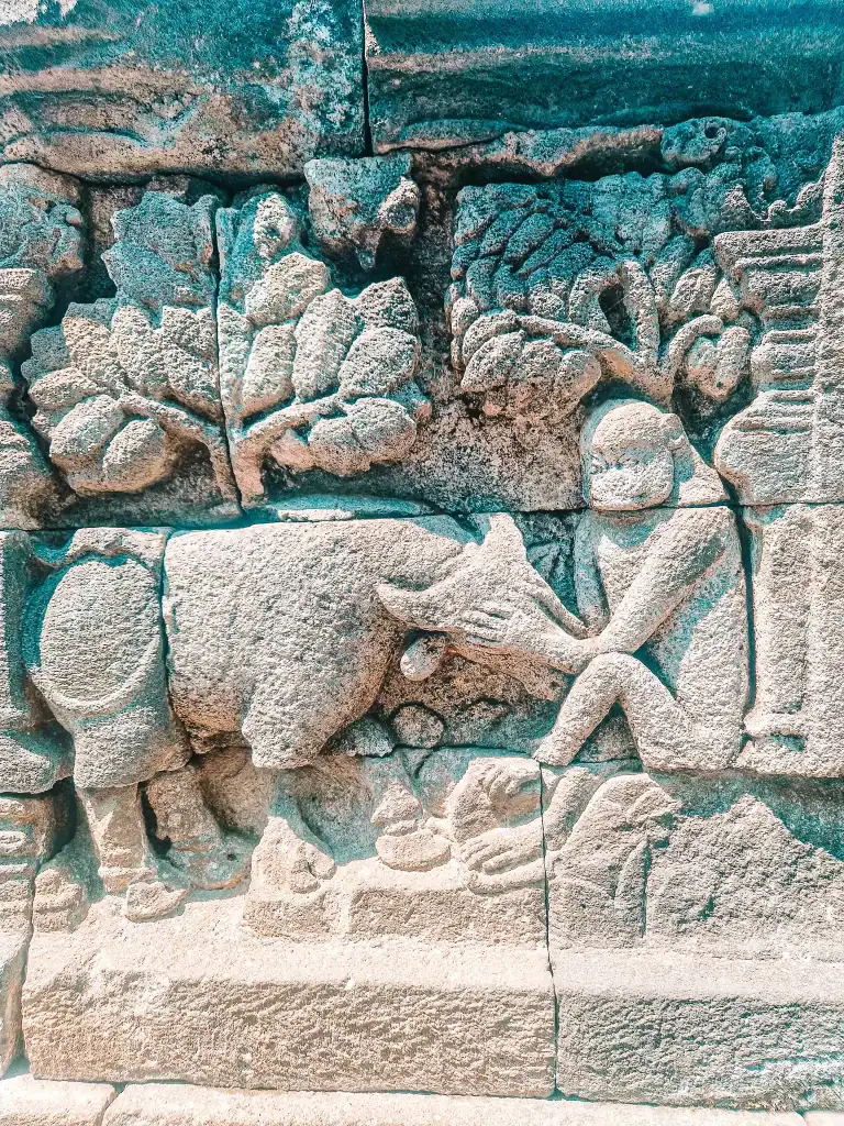 Ancient stone relief at Borobudur Temple showing a human figure interacting with an animal under carved trees, illustrating the temple’s rich storytelling tradition. A close-up like this helps travelers understand what to look for when learning how to visit Borobudur with deeper cultural appreciation.