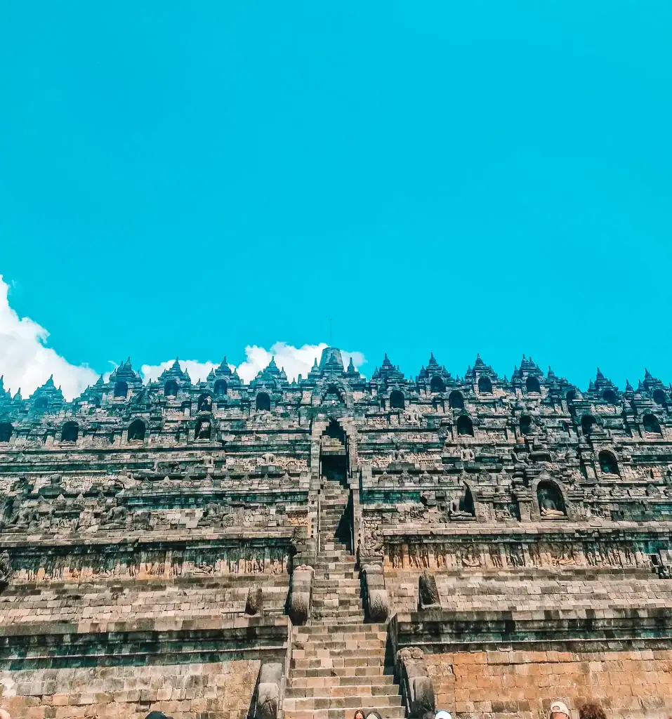 A front-facing view of the steep central staircase leading up Borobudur’s tiers, showing the temple’s symmetry and scale against a bright blue sky. Knowing what footwear and fitness level are best is key in learning how to visit Borobudur.