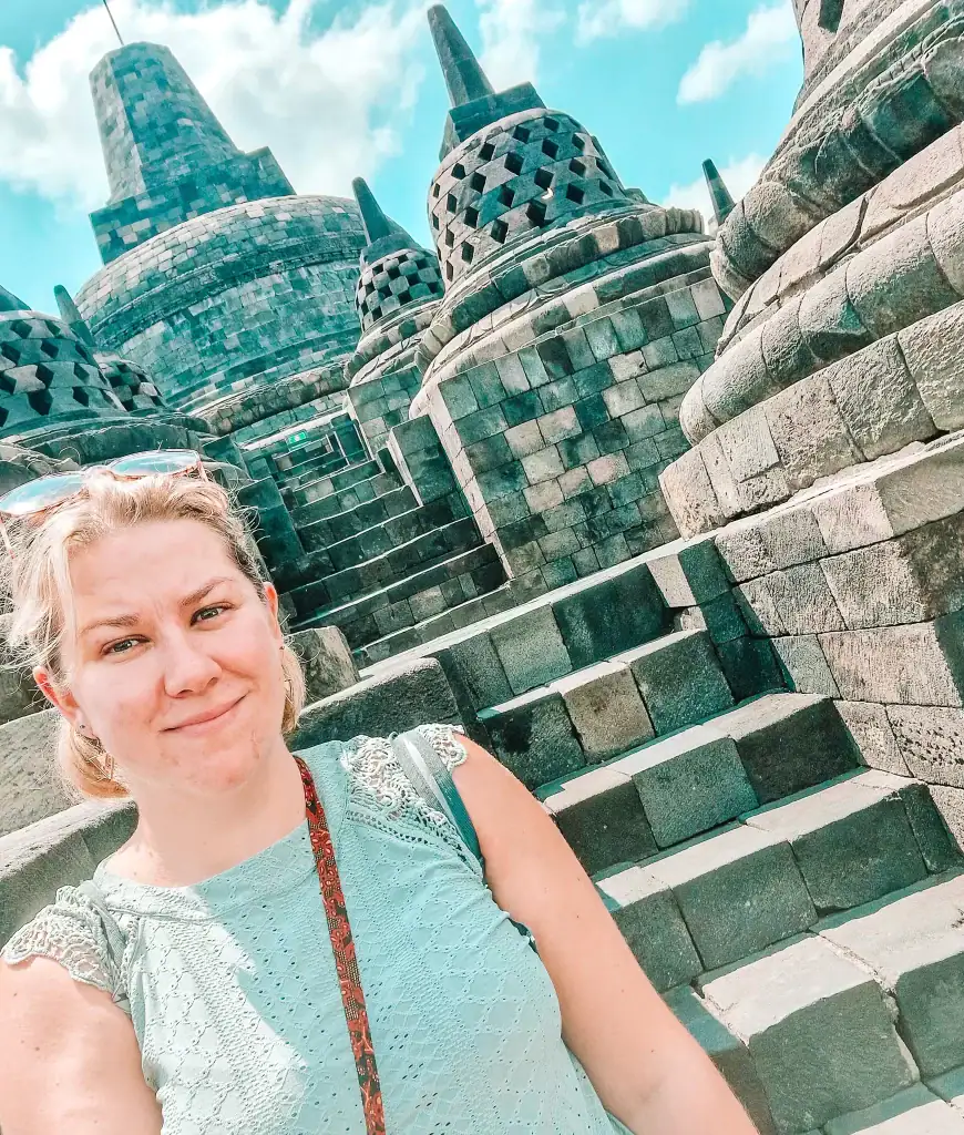 A woman takes a selfie with Borobudur’s massive central stupa behind her, framed by symmetrical smaller stupas and ascending steps. The photo reflects a personal moment at a world wonder.