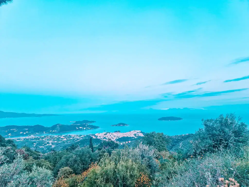 A high-altitude view from Parissis Winery in Skiathos shows a dramatic landscape of scattered islands, glowing town lights, and endless blue sea fading into dusk.
