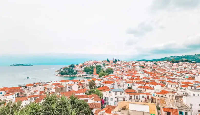 A sweeping view of Skiathos Town reveals a dense patchwork of red-roofed buildings nestled by the sea, with small islets dotting the horizon—an iconic stop among things to do in Skiathos.