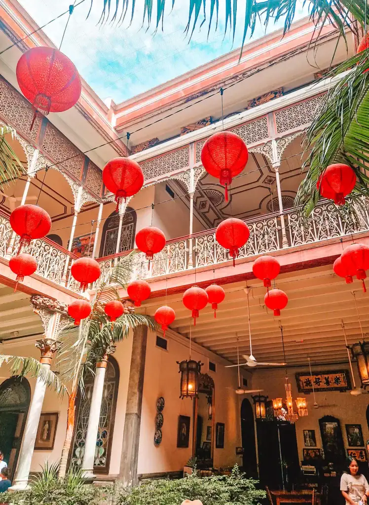 Red Chinese lanterns hang in the courtyard of the historic Blue Mansion in George Town, casting a warm glow over its ornately detailed upper balcony and colonial-style columns.