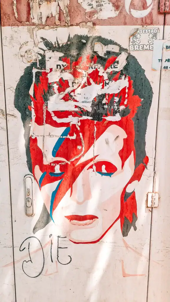 A fading street mural of David Bowie in his iconic Aladdin Sane makeup, partially torn and layered with posters and graffiti. A moody piece of Tirana’s street art scene seen during 48 hours in the city.