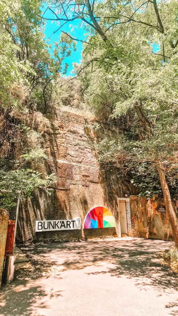 Surrounded by trees, the bunker’s exterior blends into a rocky hillside, with a colorful half-circle mural and a sign reading “BUNK’ART 1”—a must-see during 48 hours in Tirana.
