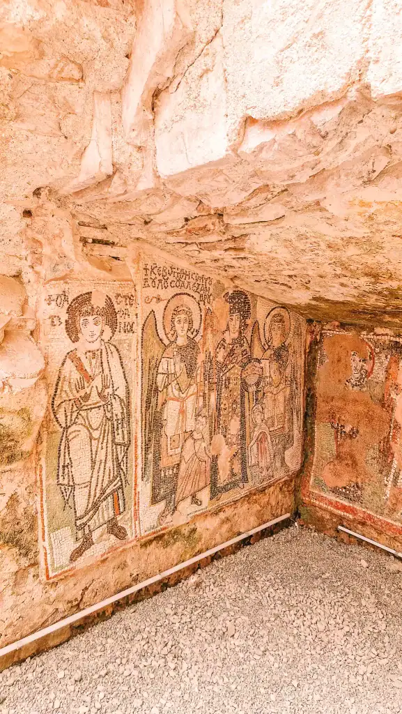 Detailed mosaic of religious figures with Greek text, preserved on the wall of a stone structure, showcasing Byzantine-style artistry.