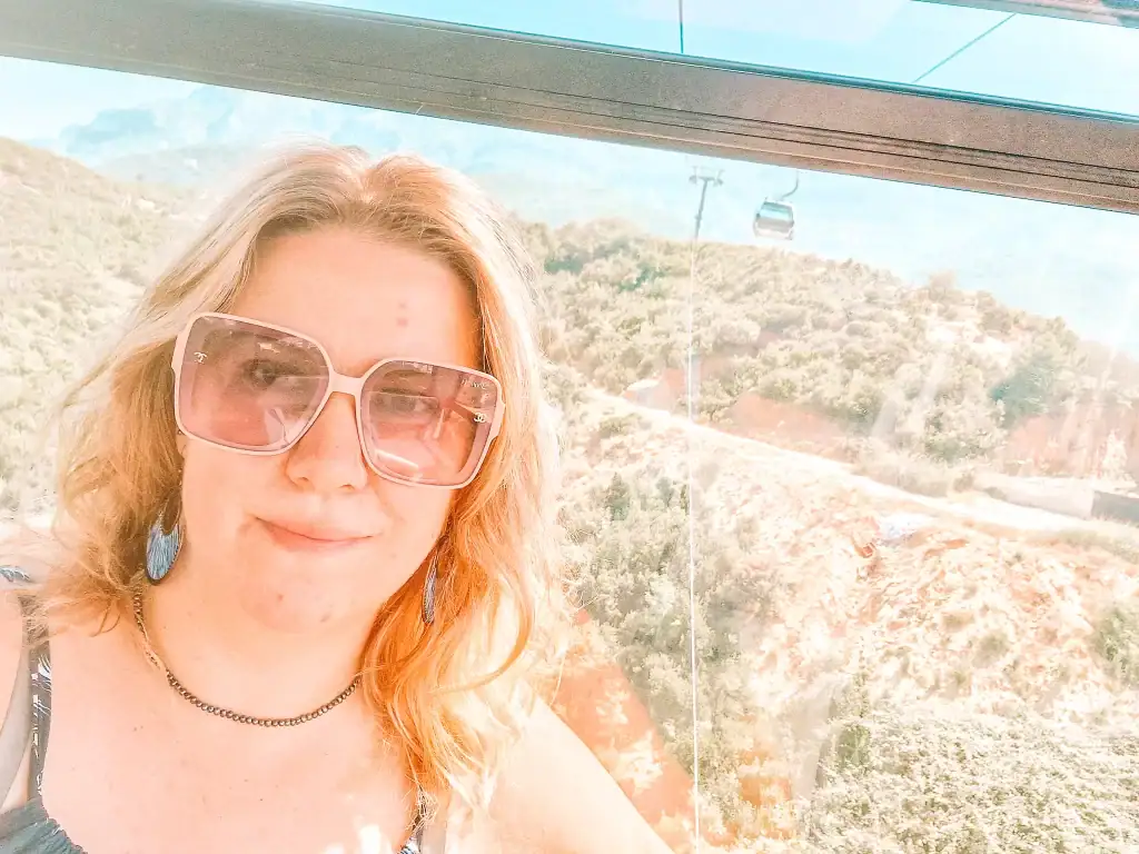 Em takes a selfie in a sunlit cable car, with panoramic mountain scenery and a gondola in the distance—a perfect way to enjoy nature in 48 hours in Tirana.