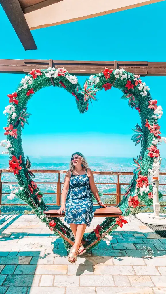 Em smiles while sitting on a bench framed by a giant floral heart, with a sweeping view of Tirana behind her—an Instagram-worthy moment from 2 days in Tirana.
