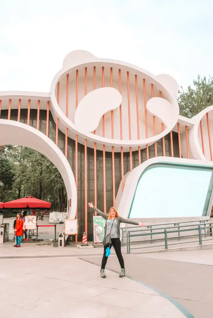 A woman stands joyfully in front of the entrance to a panda-themed building at the Chengdu Research Base of Giant Panda Breeding in China.