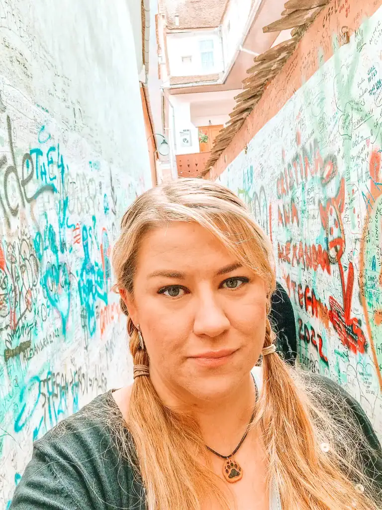 Em stands in a graffiti-covered alleyway in Brașov, surrounded by layers of scribbled names and street art—a quirky stop on a walking tour of the city's lesser-known corners.