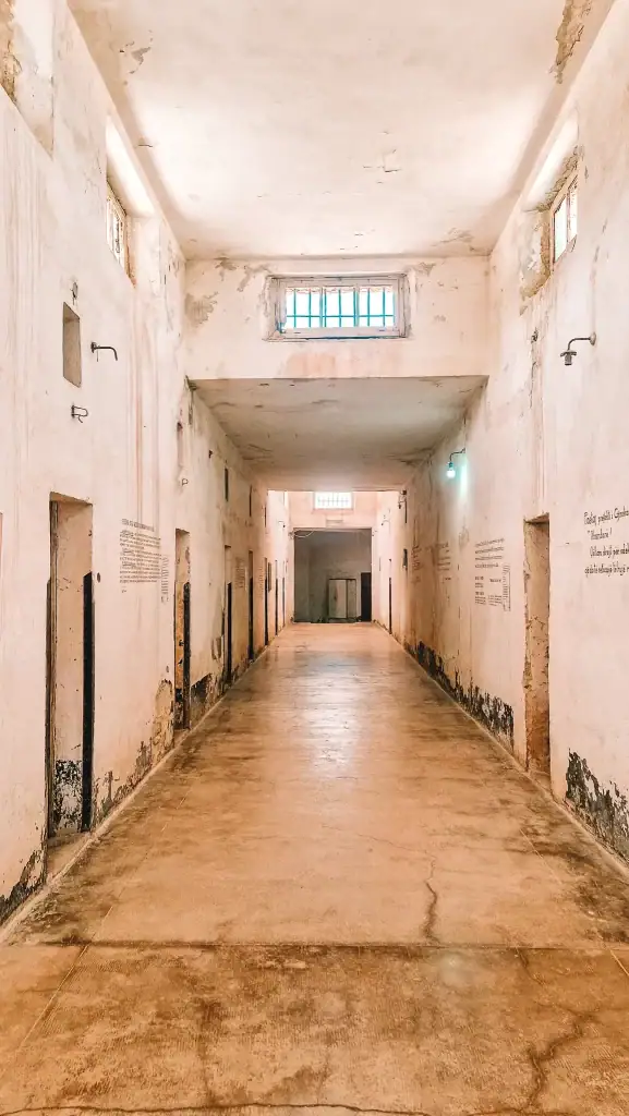 The interior of Gjirokaster's former prison, showing a long corridor with barred cell doors and peeling paint, part of the city’s dark Communist history.