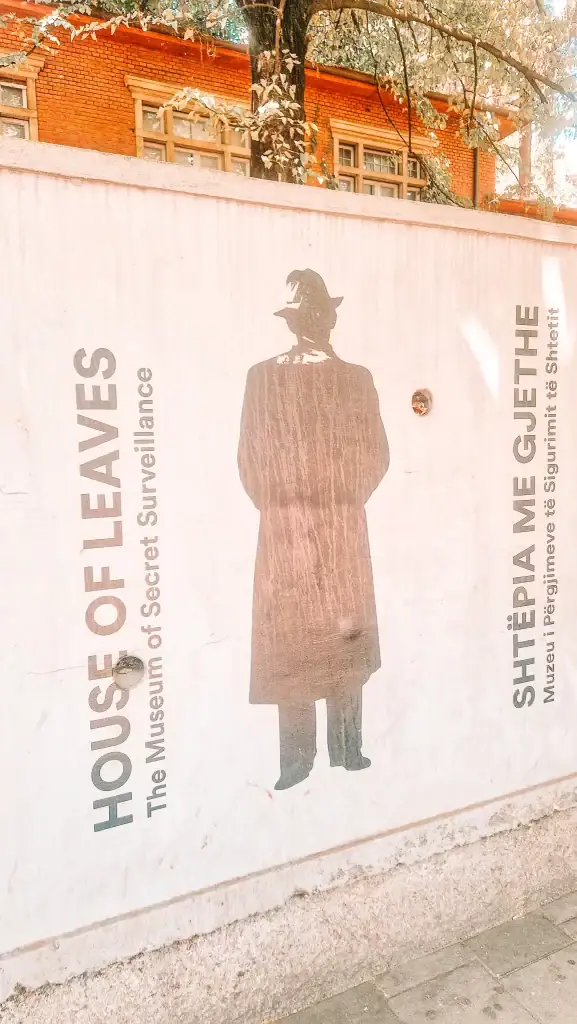 The exterior wall of the House of Leaves Museum, featuring a silhouette of a man in a trench coat and the text “Museum of Secret Surveillance” in English and Albanian.