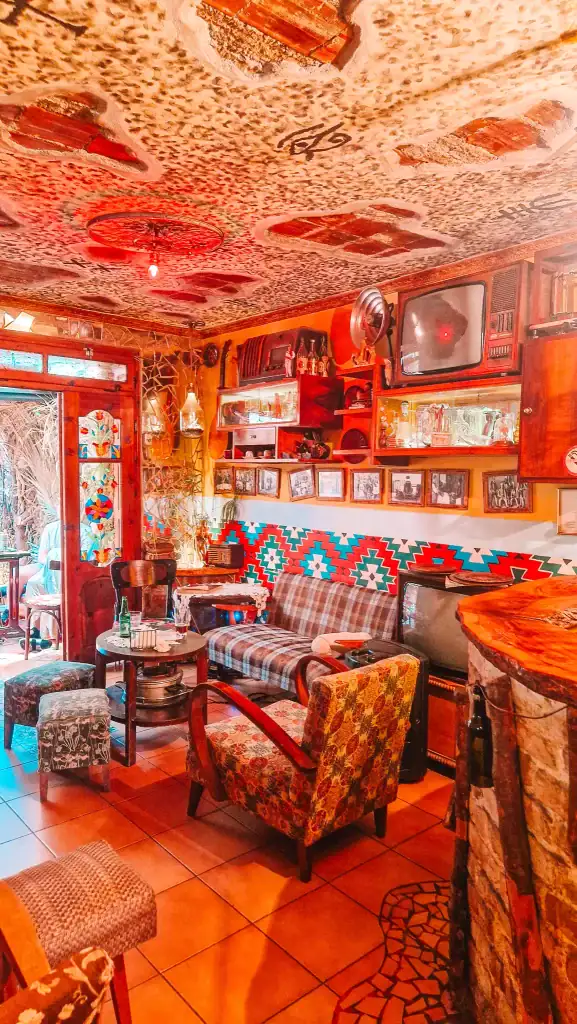 Inside Komiteti Café in Tirana, filled with vintage armchairs, patterned rugs, and mismatched decor pieces. The eclectic ambiance, with old TVs and radios, makes it one of the most unique cafes in Tirana for a nostalgic coffee break.