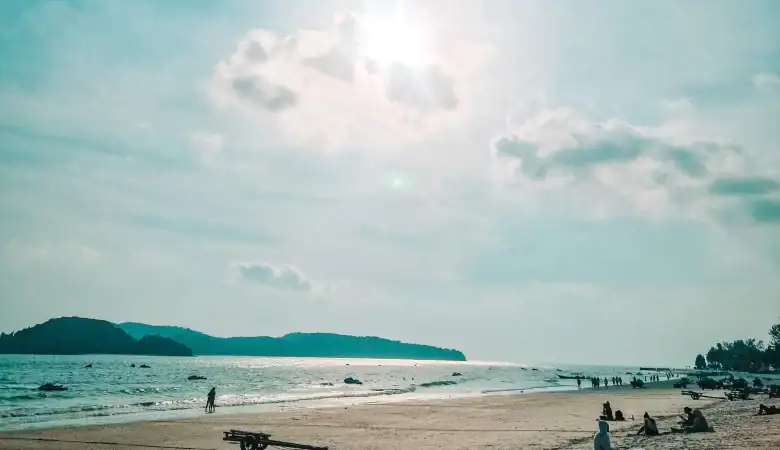 The sun glows above Pantai Cenang’s long sandy beach, where people lounge and stroll along the peaceful shoreline—Langkawi island vibes at their best during a 3 week Malaysia itinerary.