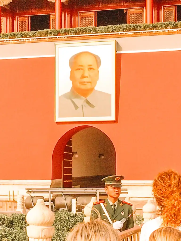 The iconic portrait of Mao Zedong above the entrance to the Forbidden City in Beijing, with a uniformed guard standing nearby.