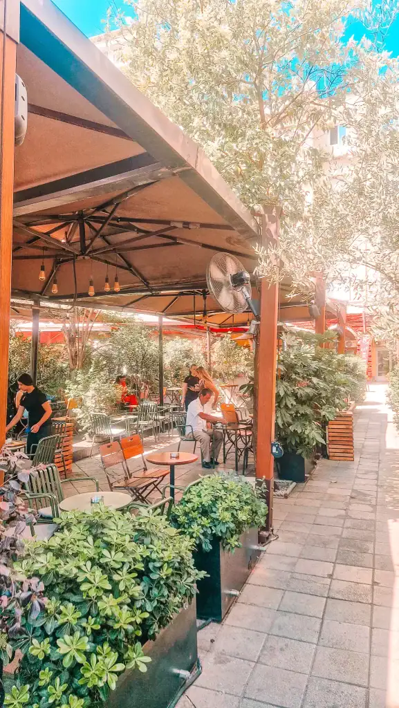 Outdoor seating at Mulliri i Vjetër in Tirana, shaded by large canopies and surrounded by lush green plants. Customers relax under the fans while enjoying coffee in one of the more established cafes in Tirana.