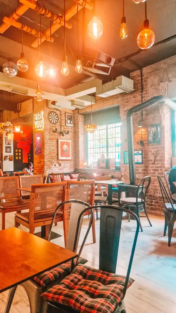 Warm and artsy interior of Noor café in Tirana with exposed brick walls, Edison bulbs, and cozy furniture. Retro decor and natural light give this café serious personality and charm.