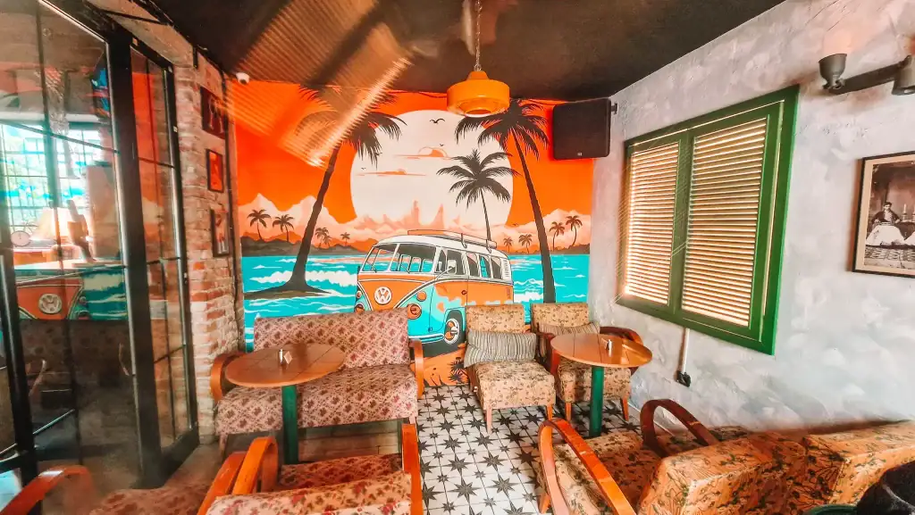 Bright and eclectic mural of a beach scene with a vintage van decorates the cozy corner nook of Noor Café’s outdoor seating area in Tirana. Tropical and retro vibes make it a hidden gem in the city’s café scene.