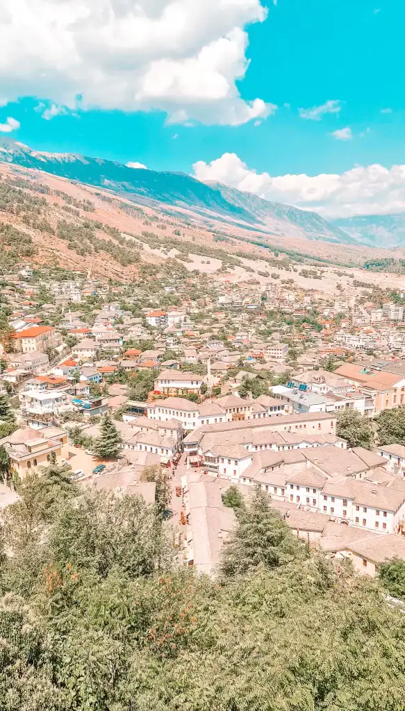 A bird’s-eye view of Gjirokaster's historic town, showing white Ottoman-style homes and narrow streets nestled at the base of a mountain range.